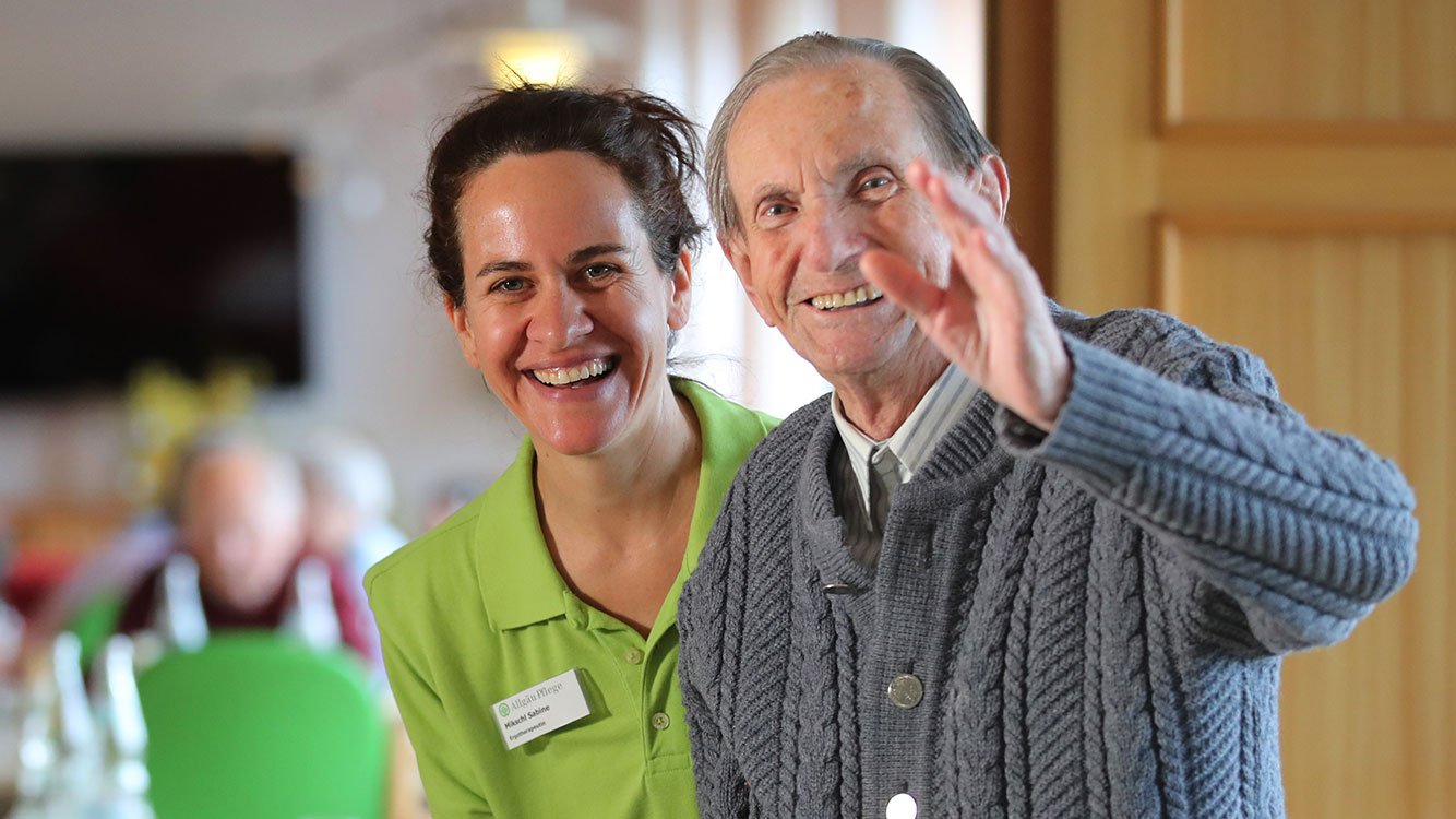 Ein Mitarbeiter der AllgäuPflege und ein Senior lächeln