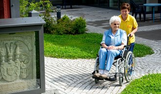 Eine Mitarbeiterin der AllgäuPflege schiebt eine Bewohnerin im Rollstuhl durch die Stationäre Einrichtung in Immenstadt
