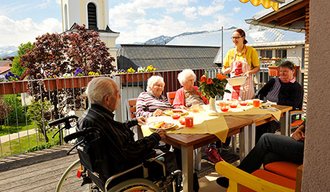 Senioren sitzen auf einem Tisch der AllgäuPflege draußen zusammen